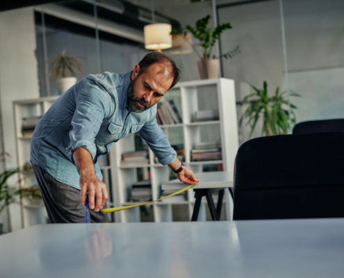 Man measuring distance between office tables