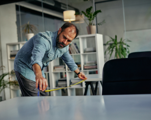 Man measuring distance between office tables