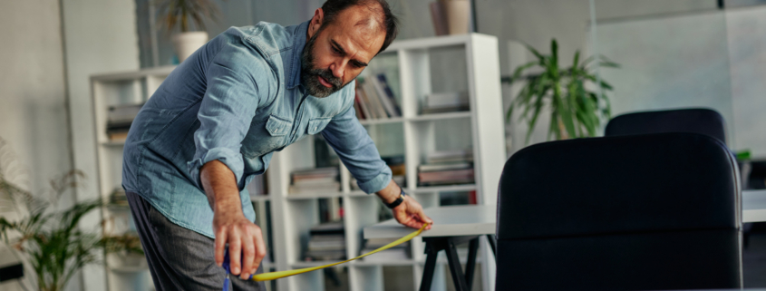 Man measuring distance between office tables